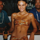 Woman in leopard print bikini holding a beer at a bar with two men behind her.