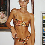 Woman wearing a leopard print bikini in an indoor setting with a shelf and decorative items.