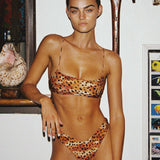 Woman wearing a leopard print bikini in an indoor setting with a shelf and decorative items.