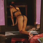 Person in a bikini standing in a doorway with a dog on a red cushion.